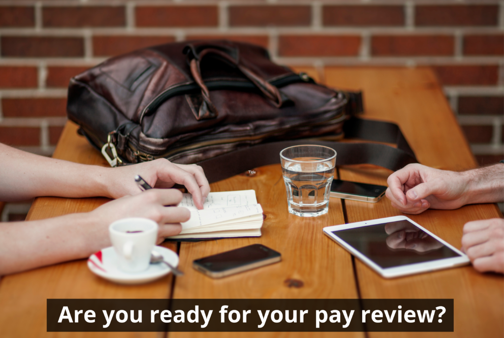 Pay review meeting: Two people at a table with a tablet, phones, coffee, and a notebook. Text: Are you ready for your pay review?