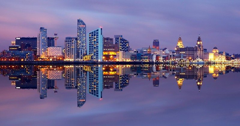 Liverpool skyline at dusk, reflecting in the water, with city lights.