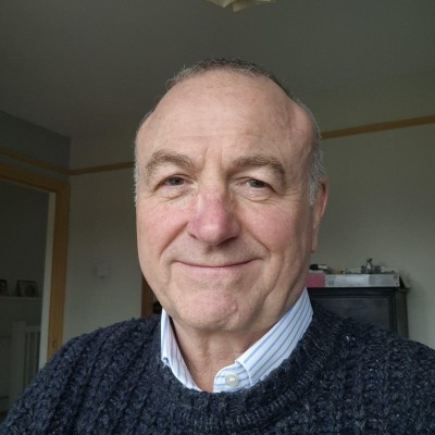 Gray-haired man in a knit sweater smiles for the camera