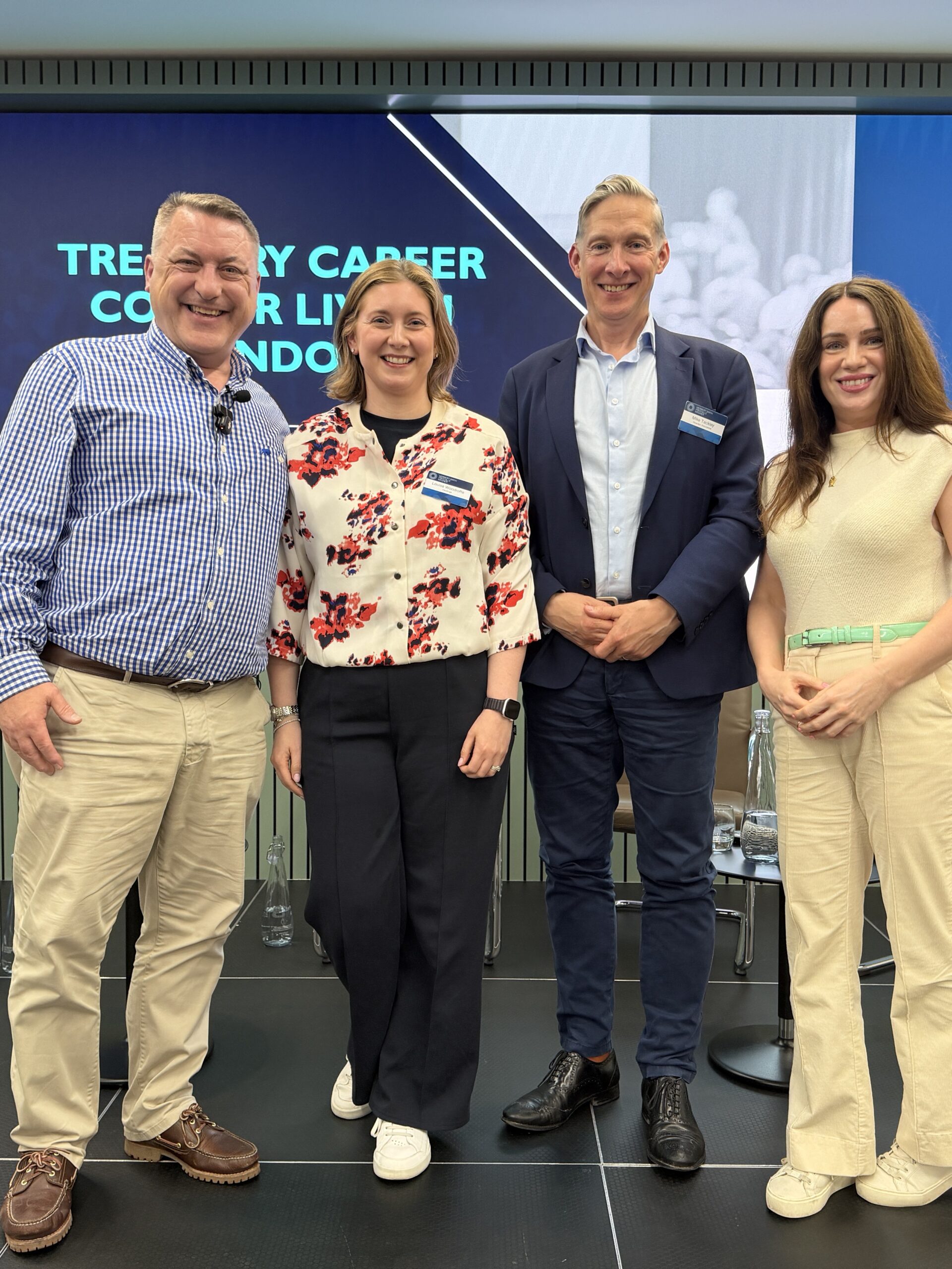Four people pose for a photo in front of a screen with "TREASURY CAREER CONFERENCE LONDON" text.